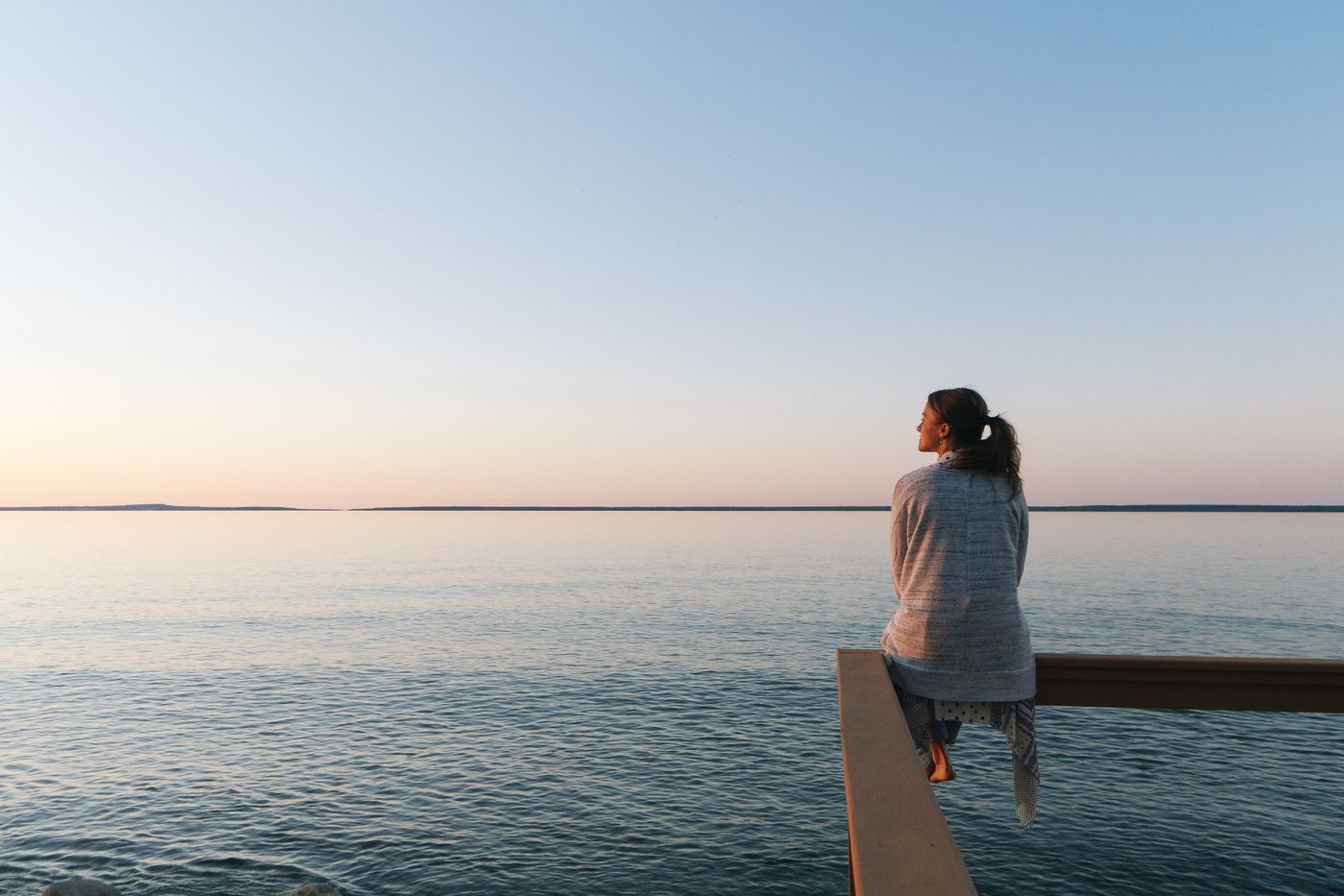A person looking out over calm water at sunrise